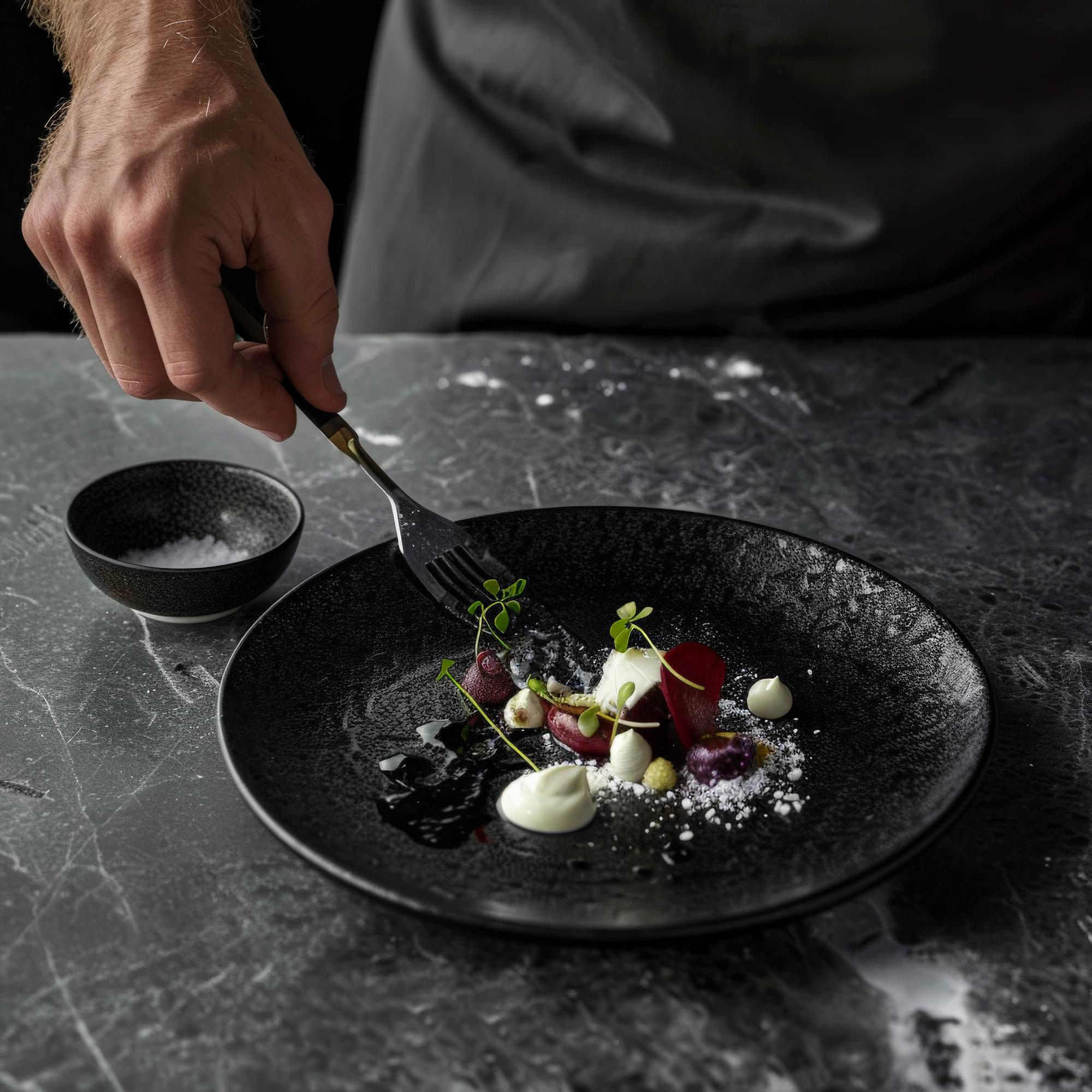 Chef plating a refined dish in a dark elegant kitchen